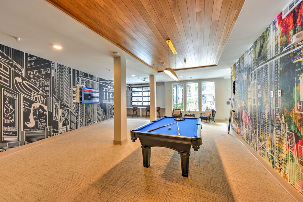 A recreation room with a pool table, wall mural, TV, and windows.