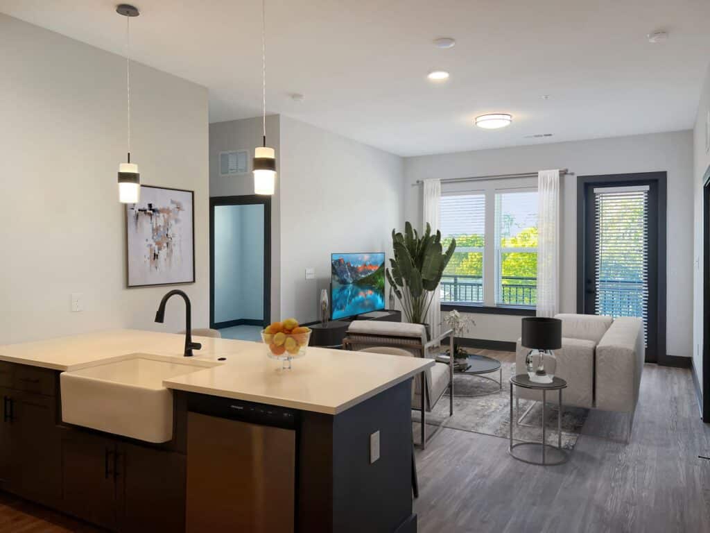 Modern living room and kitchen with a light color palette. Features include a wide sink, minimalist furniture, a TV, and large windows with natural light.